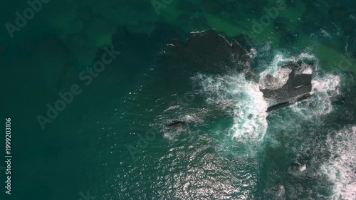 Aerial shot of the ocean with waves doing swirls and patters, rocks, sand and beach