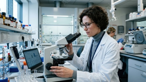 A female scientist in a lab coat examines a microscope in a well-equipped laboratory.