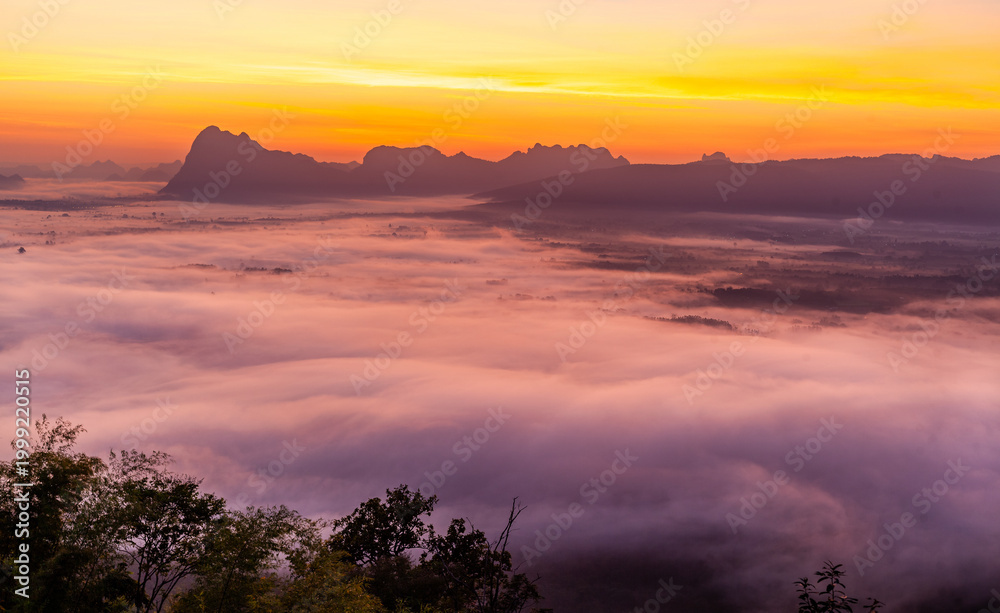 Naklejka premium Phu Kradueng National Park sunrise. Misty landscape over mountains at dawn. Thailand's natural beauty. Golden sunlight breaking through clouds.