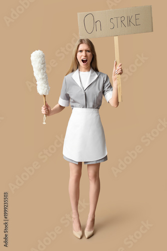 Tableau sur toile Protesting female chambermaid holding pp-duster and placard with text ON STRIKE