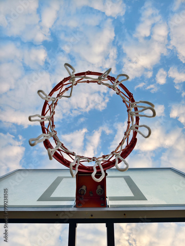 Outdoor basketball rim and net shot from a low angle perspective. Featuring a stunning blue sky background with golden hour clouds. Perfect for sports, motivation, and lifestyle concepts.