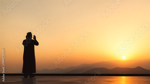 Silhouette of a person in traditional attire praying at sunrise or sunset with hands raised towards the golden sky and distant mountains.