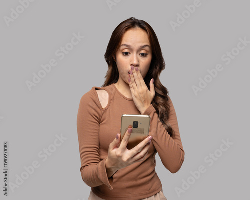 Young woman covering mouth in shock while looking at smartphone