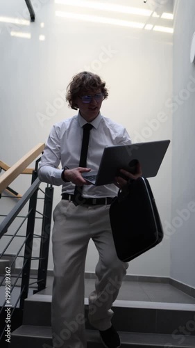 Vertical screen office worker walks on stairs using laptop and phone juggling tasks after intense workday facing burnout job loss stress failed projects and pressure adapting to digital overload and c