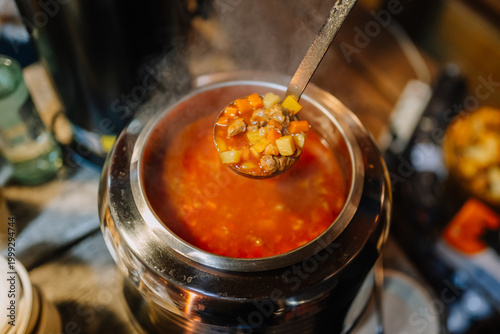 Konstfotografi Bowl of hearty vegetable soup being served from a stainless steel pot with steam
