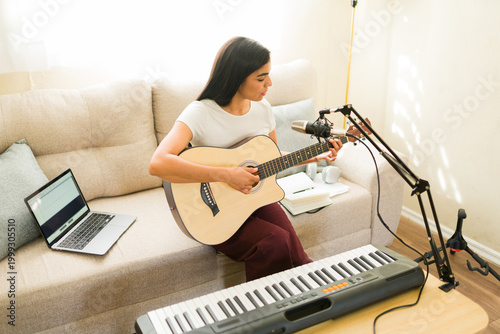 Canvastavla Latin woman composing music at home, playing acoustic guitar and recording song