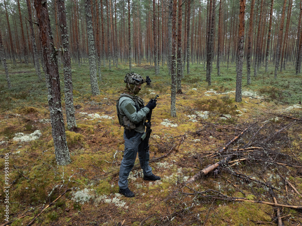 Fototapeta premium Tactical drone operator in full gear conducting forest reconnaissance using remote controller, with night vision monocular in transport position