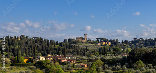 Scenic Tuscan Landscape In Florence Italy With Rolling Green Hills Cypress Trees Olive Groves Historical Villas And A Medieval Stone Tower Under A Blue Sky