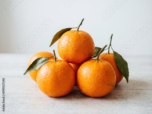 A small group of fresh ripe mandarins with green leaves on a light wooden table