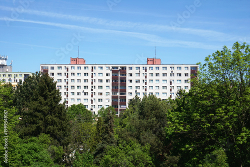 Residential Apartment Building Block Surrounded by Lush Green Trees Under Clear Blue Sky, Typical Eastern European Housing Estate Architecture, Modern Urban Living and Real Estate Background Detail.