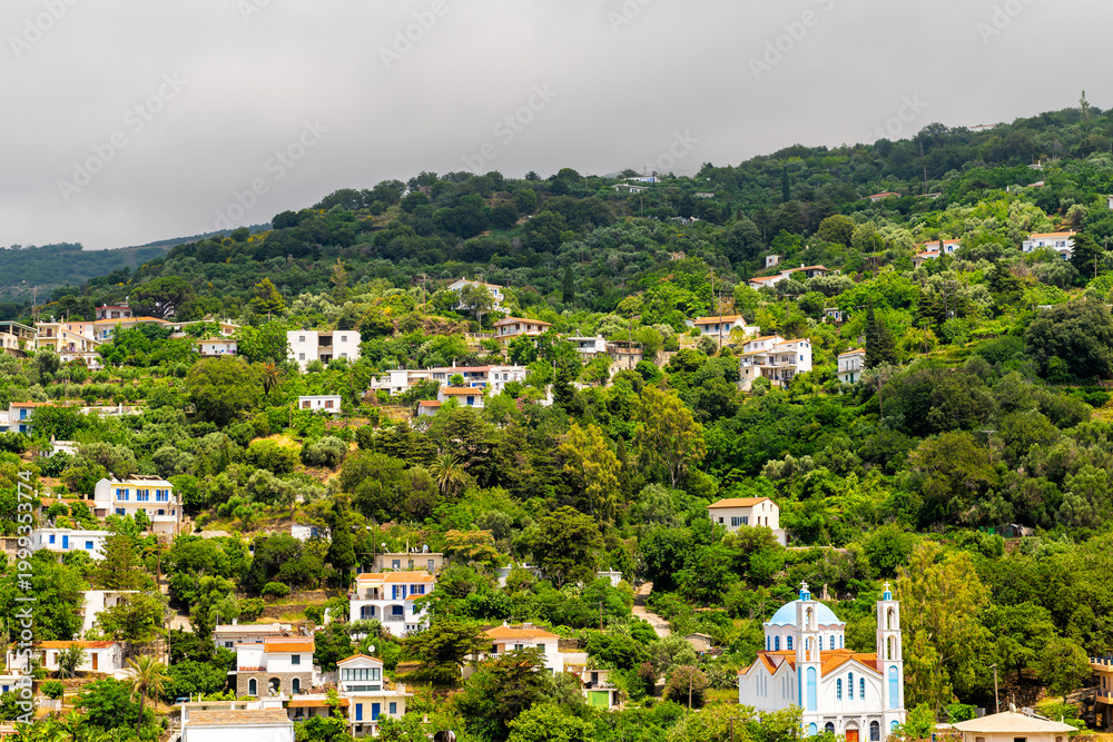Obraz premium Karavostamo, Ikaria Greek fishing village cityscape with rolling hills mountain houses homes of Aegean island longevity blue zone at sunset