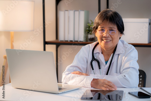 Portrait senior asian doctor woman working on laptop computer on desk in clinic, elderly female physician online consultation with medical, assistance or support with medical.