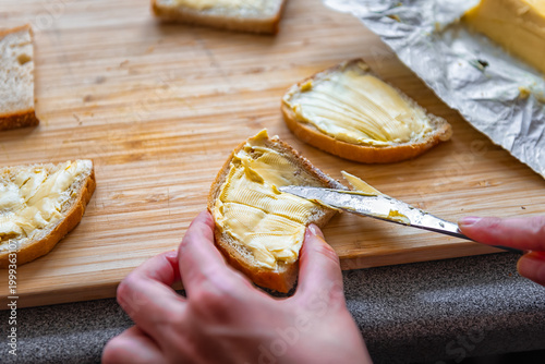 Butter bread sandwich with female woman hand spreading dairy fat with knife on wooden cutting board at home kitchen macro closeup