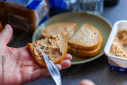 Tuna salad sandwich, woman hand spreading seafood fish spread with knife at home kitchen with table plate macro closeup