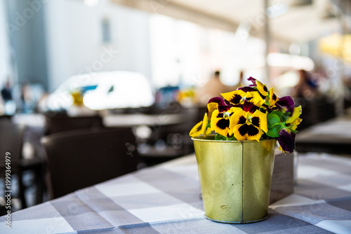 Restaurant sidewalk cafe wooden table tablecloth and yellow pansies flowers pot plant in Warsaw, Poland old town in blurry blurred background