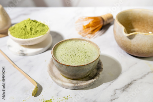 Matcha tea and powder in a bowl with bamboo whisk and spoon.