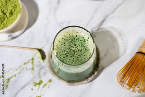 Fresh matcha tea with smooth foam served in a glass, accompanied by bamboo whisk and spoon.