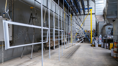 Photos Intérieur d'un atelier industriel moderne présentant des cadres métalliques blancs suspendus sur rails pour un processus de peinture et de séchage méthodique
