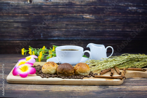 Still life coffee scene with cup of black coffee, bread, coffee beans, sunflower and cinnamon on wooden background, warm cozy cafe