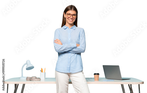 Bossy female project manager with crossed arms in glasses standing near table with laptop
