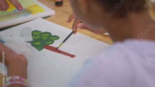 Focused student painting a tree on canvas in classroom art activity, representing creativity and concentration