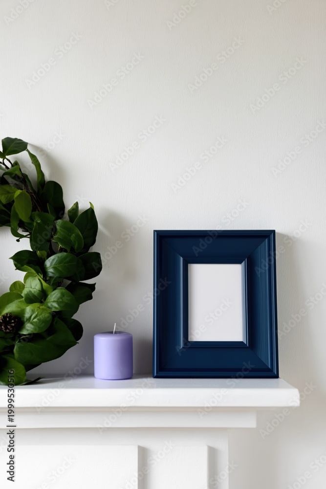Obraz premium Empty blue frame standing on mantel with candle and foliage