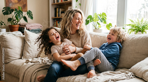 Woman laughing while playing with two children on a sofa indoors  