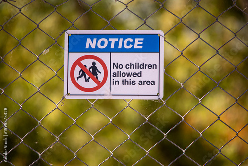 A sign on a chain link fence indicating children are not allowed on an area
