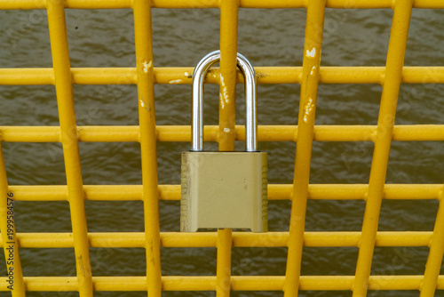 Quadro em tela Close-up of a sturdy, well-worn golden padlock securely fastened to a vibrant ye
