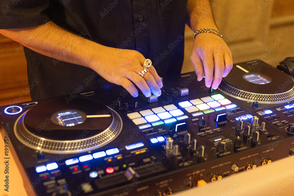 Obraz premium DJ mixing music on professional controller with illuminated pads in nightclub environment.