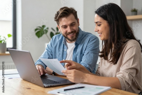 Cheerful young couple reviewing documents together on a laptop at a wooden desk