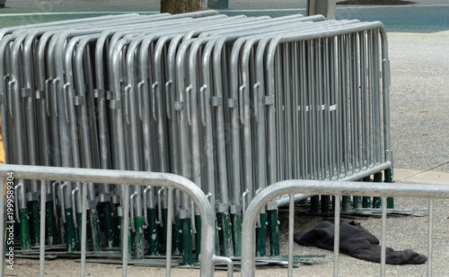 Canvas Print Compactly stacked galvanized steel crowd control barriers with green bases, organized on a paved outdoor surface, ready for temporary event management, security, or construction zone demarcation