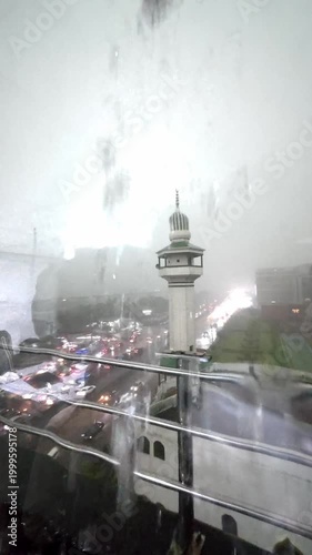 Heavy Monsoon Rain Cascades Down Glass Window Overlooking a Busy City Street with Mosque Minaret and Traffic at Dusk