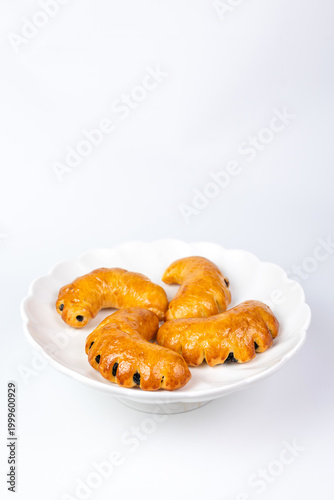 Close-up of golden crescent rolls with raisins on a white decorative plate.
