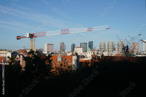 Industrial Tower Crane Over City Skyline with Modern Skyscrapers and Traditional Red Roofs, Urban Development and Construction Site in European Old Town, Real Estate Growth and Cityscape Background. 