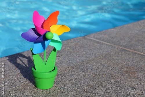 
Colorful windmill in the shape of a potted flower with a swimming pool in the background. Garden decoration.