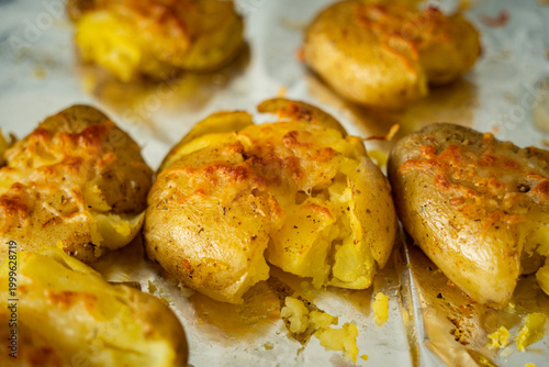 Crispy smashed potatoes with golden melted cheese on baking parchment, fresh from the oven. Rustic homemade comfort food.