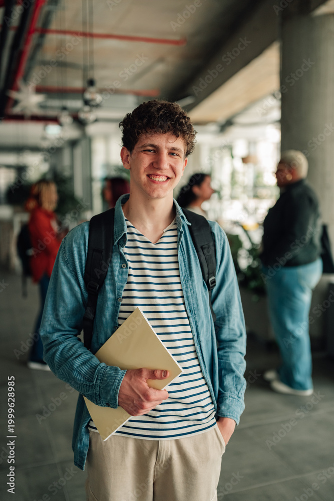 Fototapeta premium Young male student holding book, smiling at university campus, representing education, youth, and learning