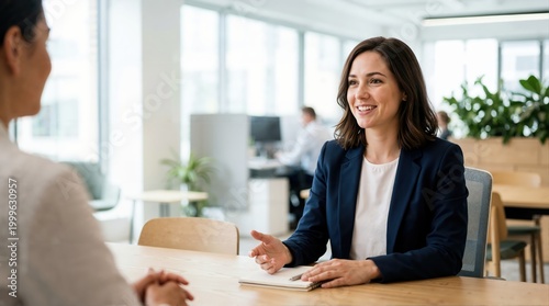 Smiling female assistant talking during a job interview in a modern office. Professional businesswoman with notebook conducting a meeting at desk. Human resources and recruitment concept
