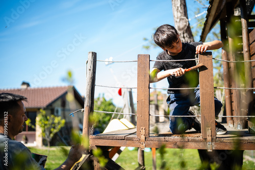 Принти на полотні Father and son building wooden treehouse together