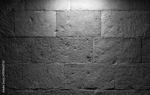 Photography A close-up view of a rough gray stone wall illuminated from above, revealing gritty textures and grayscale tones