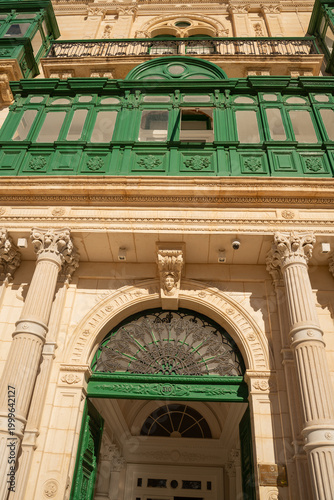Vertical view of a traditional green wooden balcony and ornate limestone columns in Valletta, Malta.
