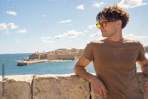 Stylish man in sunglasses with Fort Ricasoli in the background. Mediterranean lifestyle and historic fortifications in Valletta, Malta.