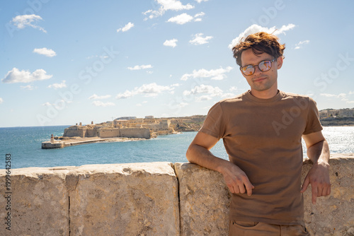 Stylish man in sunglasses with Fort Ricasoli in the background. Mediterranean lifestyle and historic fortifications in Valletta, Malta.