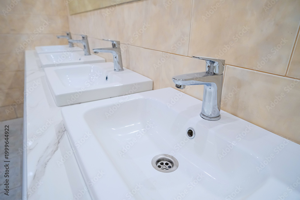 Fototapeta premium Several new and clean sinks with the same shiny chrome faucets are lined up in a row.