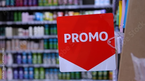 Close up of a red promotional sign swinging in a supermarket aisle with shelves of beauty and cosmetic products blurred in the background, signaling a special offer or discount on items