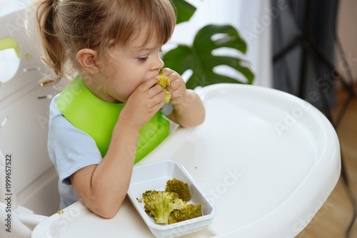 Cute little girl eating broccoli, vegetables for children as a source of vitamins, healthy lifestyle, vegetarian