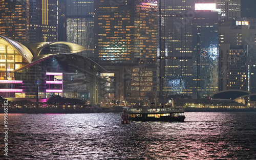 A classic Star Ferry crosses Victoria Harbour at night in Hong Kong, illuminated against a backdrop of glowing skyscrapers. 