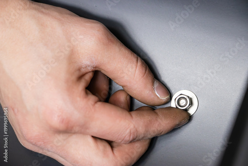 Fotografie Close-up of a male hand tightening a metal bolt on a gray surface, showcasing de