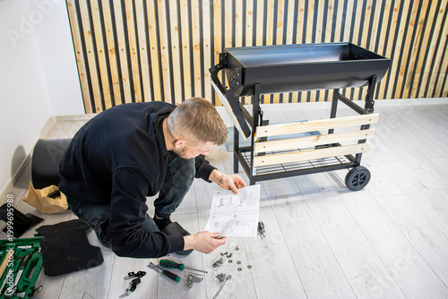 Foto Male individual assembling a black metal barbecue grill using instruction manual